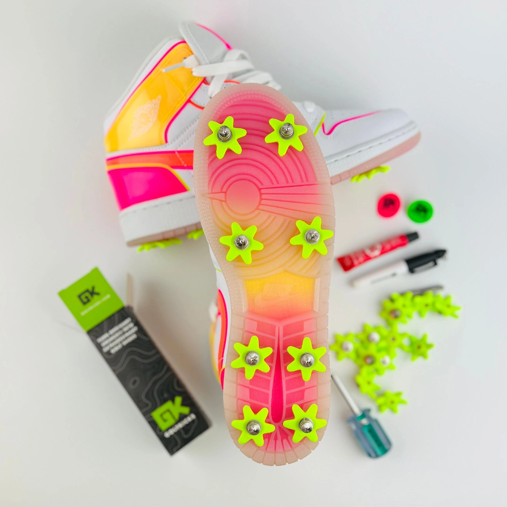 Pink sneaker soles with lime Golfkicks spikes, the Sharpie and the kit tools laid around them