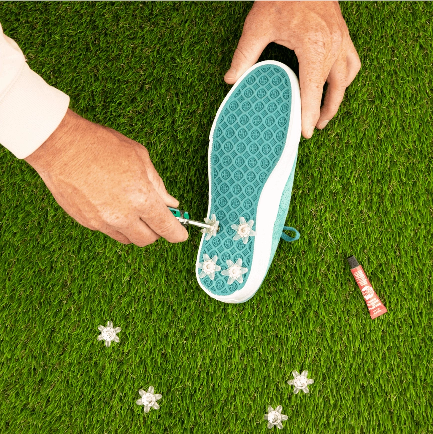 Hands screwing a spike into the sole of a teal sneaker on the grass
